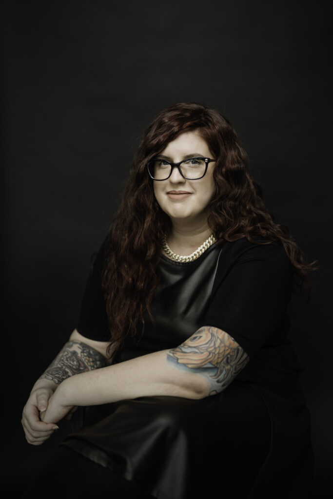 Edgy professional headshot of girl with tattoos with black background. 